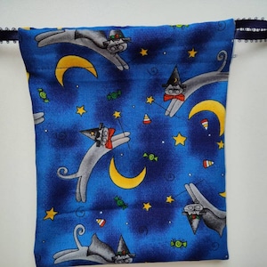 May include: A blue drawstring bag with a whimsical pattern of cats wearing witch hats and flying through a starry night sky with crescent moons and candy corn.
