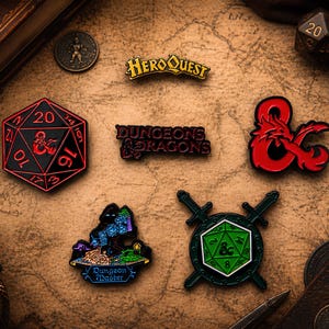 Op de afbeelding: Een verzameling emaille pins met Dungeons & Dragons en HeroQuest thema's. Inclusief een rode en zwarte D20 dobbelsteen, een rode draak ampersand, en pins met de tekst "Dungeons & Dragons" en "HeroQuest".