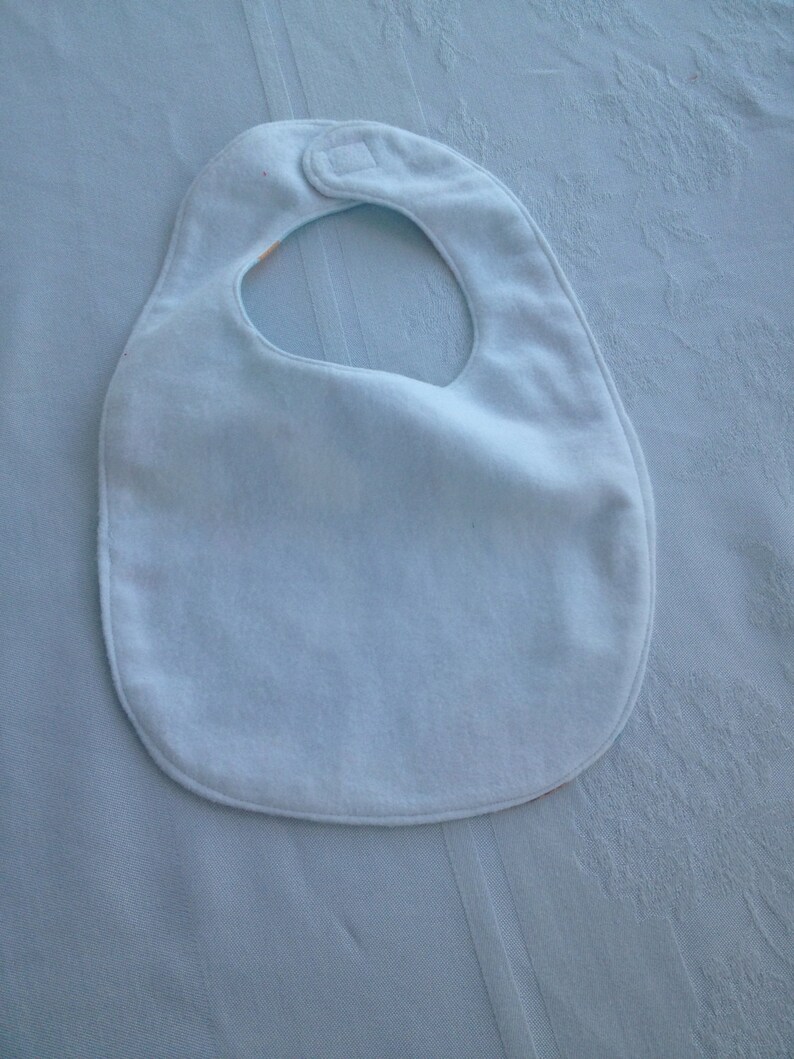 May include: A light blue baby bib with a white snap closure.