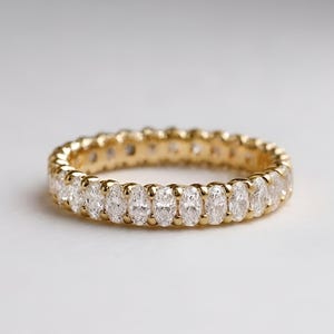 Peut inclure: Une alliance en or jaune ornée d'une rangée continue de diamants taille ovale sertis par des griffes partagées. La bague présente une finition métallique polie et une disposition uniforme de pierres facettées claires sur tout le pourtour.