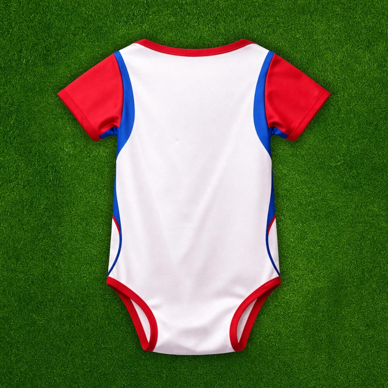 Puede incluir: Un body blanco para beb&eacute; con detalles rojos y azules. Las mangas cortas y los bordes son rojos, con rayas azules en los laterales. Este body c&oacute;modo est&aacute; dise&ntilde;ado para un uso f&aacute;cil.