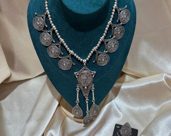 May include: A silver-toned necklace featuring a beaded chain with circular coin-like charms and a central pendant with three dangling teardrop-shaped pieces. A matching pair of teardrop-shaped earrings is displayed on a black card nearby.