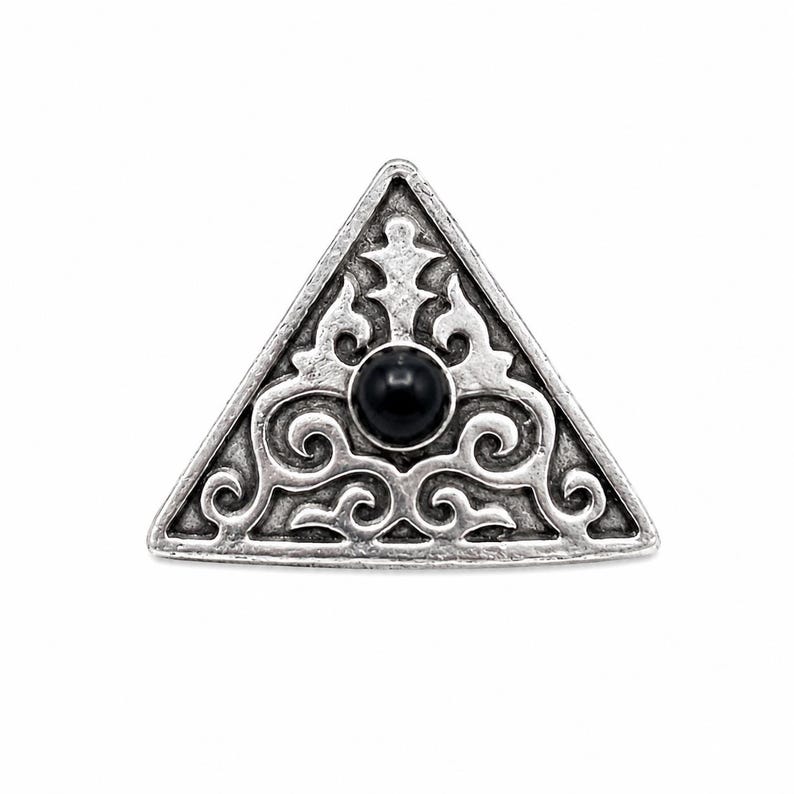 May include: A triangular silver-toned metal brooch featuring an intricate embossed scrollwork pattern and a single smooth, round black stone set in the centre. The metal has a darkened, antiqued finish that highlights the detailed relief design.