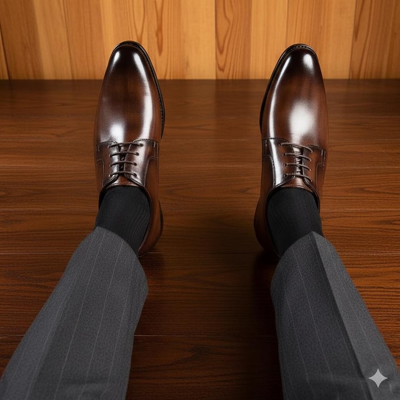 May include: A pair of brown leather dress shoes with a glossy finish. The shoes are laced up and worn with black socks and grey pinstripe trousers. The shoes are on a wooden floor.