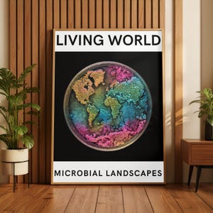 Può includere: Una stampa incorniciata con le parole "LIVING WORLD" in alto e "MICROBIAL LANDSCAPES" in basso. L'opera presenta un'immagine circolare colorata della Terra, resa in tonalità di rosa, blu, verde e oro, su uno sfondo nero.