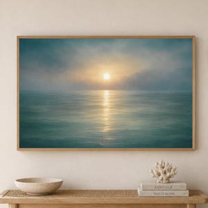 Peut inclure: Une impression d'art mural rectangulaire représentant une scène océanique sereine au lever du soleil avec une douce lumière dorée se reflétant sur l'eau, encadrée en bois clair, exposée au-dessus d'une console en bois avec un bol, des livres et une sculpture de corail.