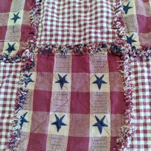 May include: A patchwork quilt with a patriotic theme. The quilt features alternating squares of red and white gingham and solid red fabric. Dark blue embroidered stars are scattered across the quilt. The edges have a frayed, textured trim.