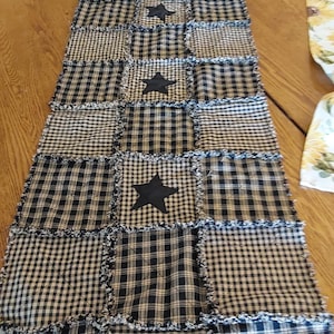 May include: A black and white checkered table runner with four black star appliqués. The runner is made of fabric squares with a frayed edge. The pattern includes gingham and plaid designs.