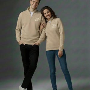 Könnte beinhalten: Zwei Personen tragen beigefarbene Sweatshirts mit Viertelreißverschluss und dem Text "YOUR DESIGN HERE". Eine Person trägt eine schwarze Hose, die andere eine blaue Jeans. Beide tragen weiße Turnschuhe. Der Hintergrund ist einfarbig grau.
