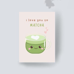 Könnte beinhalten: Eine rechteckige Grußkarte mit hellrosa Hintergrund und einer Cartoon-Illustration einer grünen Matcha-Tasse mit lächelndem Gesicht, rosa Wangen und einem weißen Herz. Der Text lautet i love you so MATCHA in brauner und grüner Schrift.