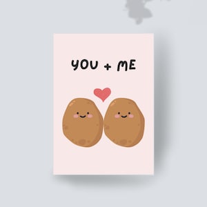 May include: A rectangular greeting card with a light pink background featuring two brown cartoon potatoes with smiling faces and rosy cheeks. Between the potatoes is a small red heart. The text YOU + ME is printed in black above the potatoes.