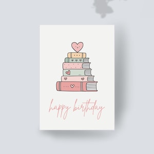 Könnte beinhalten: Geburtstagskarte mit einem Stapel Bücher in Pastellfarben, gekrönt von einem Herz. Einige Bücher haben Herzdetails. Die Worte "happy birthday" sind in einer Schreibschrift unter den Büchern geschrieben.