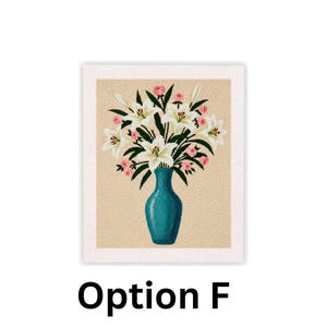 May include: A framed floral needlepoint featuring a teal vase filled with white lilies and pink roses. The background is a light tan color, and the frame is white. The text "Option F" is at the bottom.