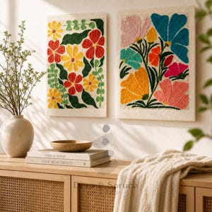 May include: Two embroidered floral wall hangings. One displays red, yellow, and green flowers, the other features pink, blue, and orange blooms. Both are framed on a neutral backdrop, adding a vibrant touch. The artwork is displayed above a wooden cabinet.