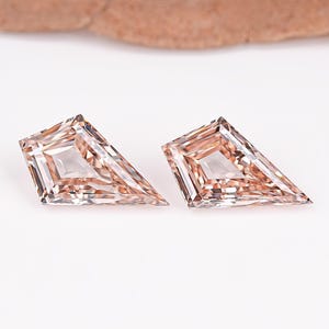 May include: Two loose kite-shaped gemstones with a light peach or champagne hue. Each stone features a faceted surface with a pointed top and a wide base, displaying internal reflections and a clear, transparent quality across the entire structure.