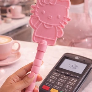 May include: A pink, double-sided Hello Kitty-shaped item with a handle is held near a payment terminal. The image features a pink color scheme, with the text "Double Sided" at the bottom.