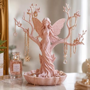 May include: A pink fairy-shaped jewelry holder with outstretched arms and wings, designed to hold necklaces and earrings. The holder has a tree-like structure with branches for hanging jewelry. The base of the holder has a small dish for rings and other small items.