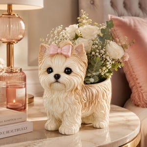 May include: A cream and tan colored dog-shaped planter featuring a light pink bow on its head. The ceramic figure has large black eyes and a textured coat, and it is filled with a bouquet of white roses and green eucalyptus leaves.