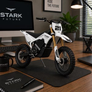 Könnte beinhalten: Ein weißes und schwarzes Stark Future Elektro-Dirtbike mit goldenen Federgabeln. Das Motorrad hat die Nummer 21 auf der Vorderseite und wird auf einem Schreibtisch mit einem Computer und Stark Future-Merchandise ausgestellt.