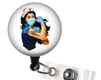 May include: A white badge reel with a round, white button featuring a cartoon image of a female nurse wearing a blue uniform, a white hat, a blue surgical mask, and blue gloves. The nurse has a red cross tattoo on her arm with the word "Nurse" written on it. The nurse is flexing her bicep.