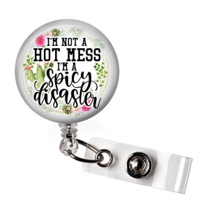 May include: A white retractable badge holder with a round, clear button featuring a floral design and the text "I'm not a hot mess I'm a spicy disaster".