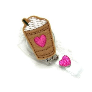 May include: A brown and white coffee cup with a pink heart on the side, attached to a retractable badge holder with a pink heart charm.