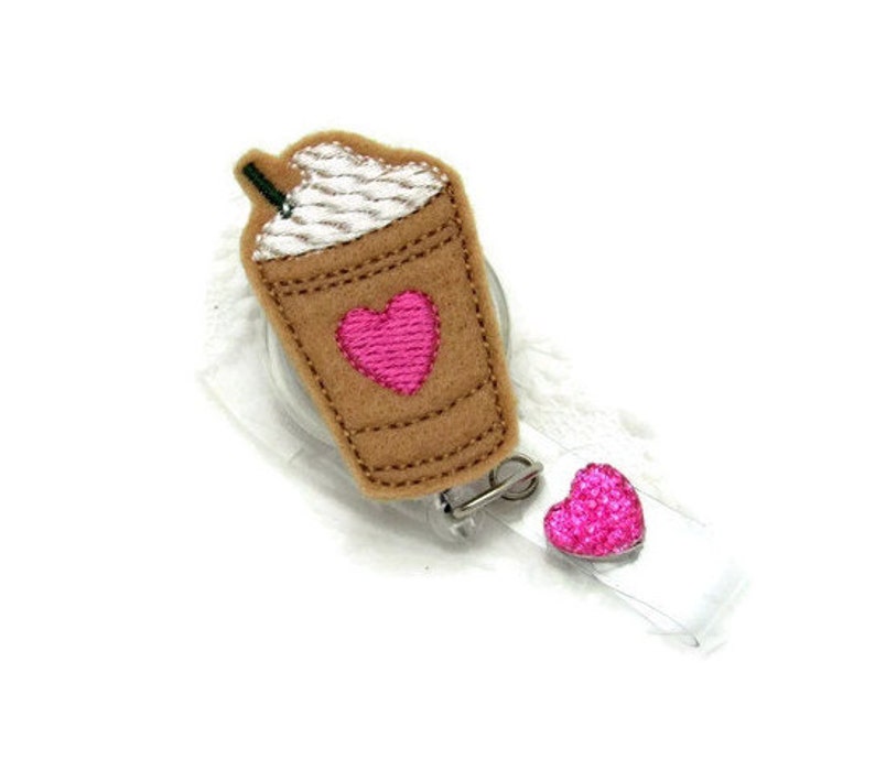 May include: A brown and white coffee cup with a pink heart on the side, attached to a retractable badge holder with a pink heart charm.