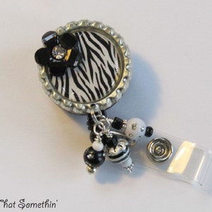 May include: A black and white zebra print badge reel with a black flower and a rhinestone center. The reel has a silver metal base and a clear plastic retractable cord.
