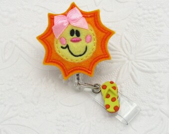 May include: A yellow felt sun with a smiling face and a pink bow, attached to a clear plastic badge holder with a yellow and red flip-flop charm.
