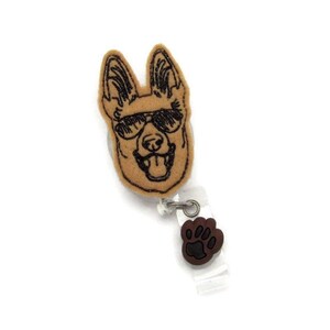 May include: A brown felt badge reel with a black and white embroidered image of a German Shepherd wearing sunglasses. The reel has a brown wooden paw print charm.
