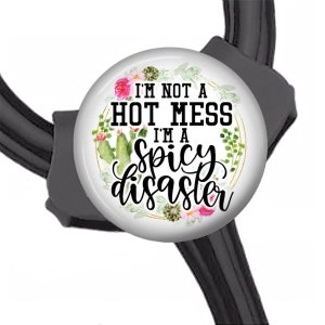 May include: A white stethoscope charm with a gold circle and floral design. The text reads "I'm not a hot mess I'm a spicy disaster".