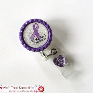 May include: Purple and white Alzheimer's Awareness badge reel with a purple ribbon and glitter. The reel has a purple heart charm.