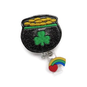 May include: Black pot of gold with a green shamrock and gold coins, attached to a rainbow and heart charm on a retractable badge reel.
