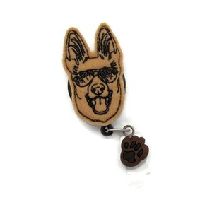 May include: A brown felt German Shepherd dog with sunglasses and a black outline is attached to a retractable badge reel with a brown paw print charm.