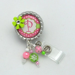 May include: A pink and green polka dot badge reel with a silver bottle cap, a green flower, and a white letter "P" in the center. The reel has a clear plastic badge holder and pink, green, and white beads.