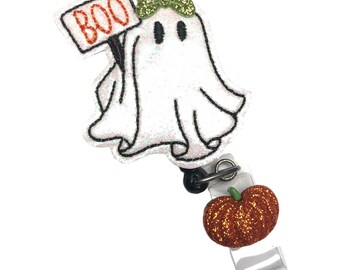 May include: A white glitter ghost with a green bow holding a sign that says "BOO" and a small orange glitter pumpkin attached to a clear badge holder.