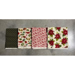 May include: Four folded fabric pieces with Christmas patterns. Designs include a black and gold geometric pattern, baubles, red berries, and poinsettias. The fabrics are likely cotton.