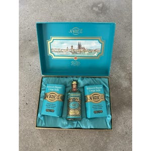 May include: A teal gift box containing a glass bottle of 4711 Echt Kölnisch Wasser and two bars of 4711 Kölnisch Wasser Crème Seife. The inside lid features a gold-framed illustration of the Cologne skyline. The items rest on teal fabric.