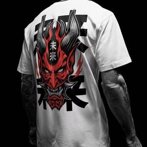 May include: A white t-shirt featuring a large graphic on the back. The design displays a red, horned demon mask with sharp teeth and grey horns. The mask is overlaid with black Japanese characters and the white text "未来" on the forehead.
