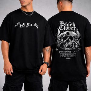 以下が含まれることがあります： 前面に英語と日本語でBlack Cloverと白文字でプリントされた黒いTシャツ。背面には、角と牙のある頭蓋骨の大きな白いグラフィックが描かれており、複雑なディテール、日本語のテキスト、Black Cloverのタイトルが添えられています。