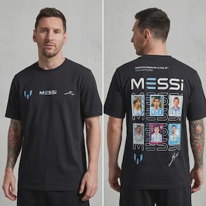 May include: A black short-sleeve t-shirt featuring the text MESSI and a logo on the front. The back displays the text COUPE DU MONDE DE LA FIFA 26, 11 juin au 19 juillet, the word MESSI, six individual player card graphics, a logo, and a signature.