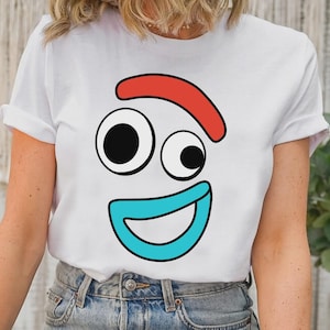 以下が含まれることがあります： 白い半袖Tシャツで、漫画の顔のグラフィックプリントが施されています。デザインには、赤い曲線の眉毛、左右非対称の黒と白の丸い目、そして胸の中央に配置された幅の広い水色の曲線の口が含まれています。