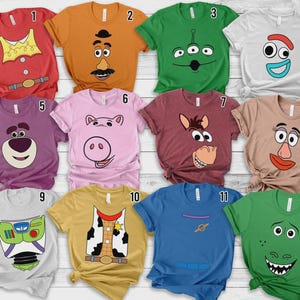 Puede incluir: Una colección de doce camisetas de manga corta con varios diseños de personajes de la franquicia Toy Story, incluyendo rostros y elementos de disfraces impresos en telas de color rojo, naranja, verde, blanco, morado, rosa, granate, tostado, gris, amarillo y azul.