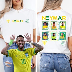 Puede incluir: Una camiseta blanca con el texto NEYMAR en amarillo y verde, el logotipo njr y una firma en la parte delantera. La parte trasera muestra el texto NEYMAR en amarillo y verde, seis tarjetas coleccionables de fútbol de Neymar y una firma verde.