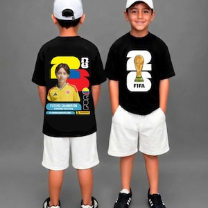 Puede incluir: Dos camisetas negras con pantalones cortos blancos y gorras blancas. La camiseta izquierda presenta un gráfico de camiseta de fútbol amarilla, el texto FUTURO CHAMPEÓN y el número 26. La derecha muestra un 26 blanco grande con el trofeo FIFA.