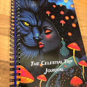 May include: A spiral-bound journal with a striking cover design. It features a wolf and a woman's face, with the text "The Celestial Trip Journal." The cover art includes red mushrooms and a starry night sky. The journal has a black spiral binding.