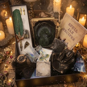 Könnte beinhalten: Eine Geschenkbox mit einer grünen Federkiel-Schreibfeder mit goldenen Federspitzen, einer schwarzen Tintenflasche, einem Buch mit grünem Drachenrelief-Einband, einem Heft mit dem Titel Spell Jar Recipes, einem schwarzen Kerzenhalter und Zubehör.