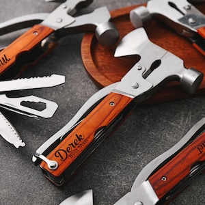May include: A collection of multi-tool hammers with wooden handles and stainless steel components. Each tool includes a hammer head, pliers, and folding blades. The handles are engraved with names such as "Michael" and "Derek Best Man".