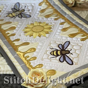 May include: Close-up of a quilted fabric with bee and sunflower embroidery. The design features a honeycomb pattern, gold honey drips, and the text "StitchDelight.net" at the bottom. The color palette includes white, yellow, gold, gray, and brown.