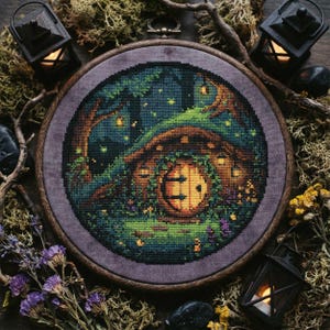 Puede incluir: Un punto de cruz de una escena de agujero de hobbit, enmarcado en un aro de madera redondo. La imagen presenta una puerta redonda de madera, rodeada de exuberante vegetación y luces brillantes. La escena está ambientada en un bosque con árboles y un cielo estrellado.